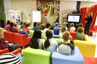 Groep kinderen op kleurrijke banken, luistert naar schrijfster